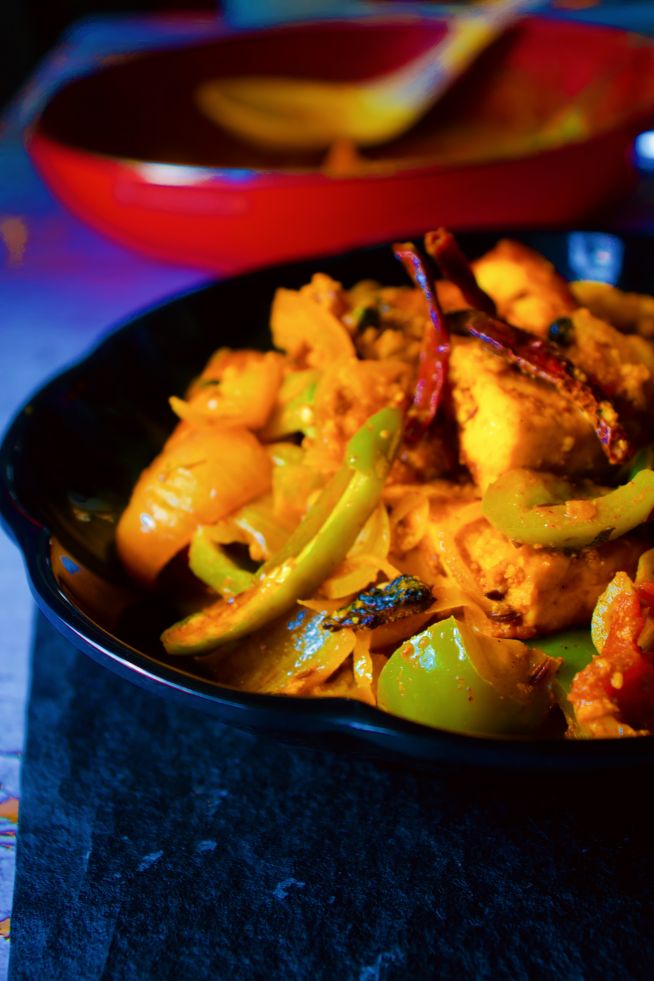 Dhaba Style Paneer Do Pyaza kept on a black plate with pan in the background