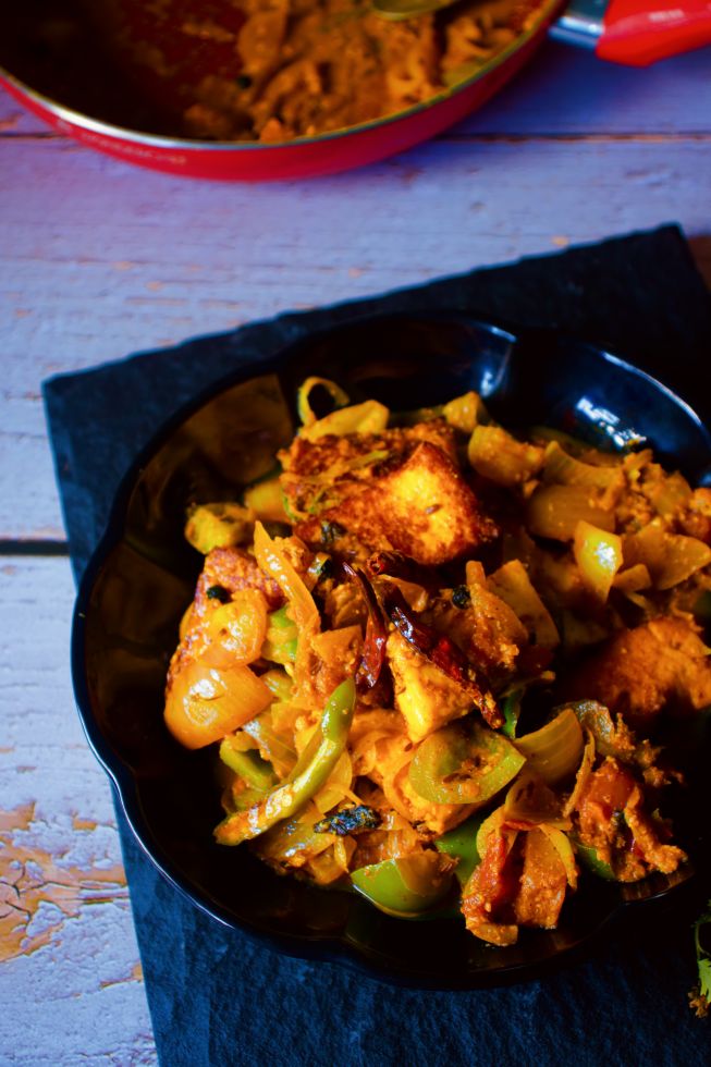 Dhaba Style Paneer Do Pyaza kept on a black plate with pan in the background