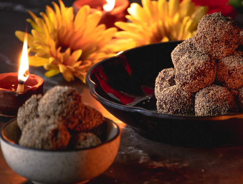 Two bowls with ladoo and yellow flower and diya in the background