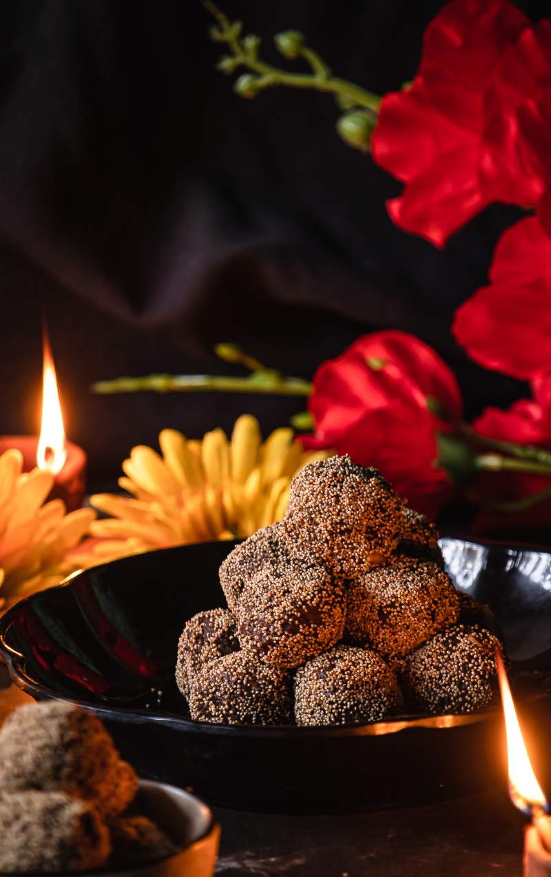 A stack of ladoo with diyas and a red flower in the back